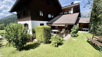 Charmantes Haus mit gepflegtem Gartenbereich und kleiner Terrasse, umgeben von üppigem Grün.