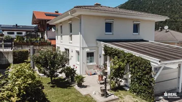 Ansicht des Hauses von der Gartenseite mit Terrasse, Carport und gepflegter Grünfläche.