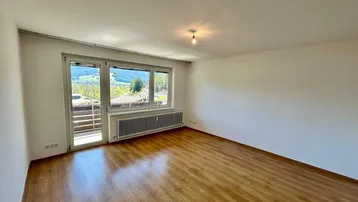 Helles Wohnzimmer mit Laminatboden, großem Fenster und Zugang zum Balkon mit Bergblick.