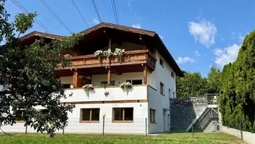 Traditionelles Haus mit Holzbalkonen und grüner Umgebung unter blauem Himmel.