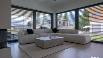 Helles Wohnzimmer mit großem Ecksofa, modernem Couchtisch und Blick auf die Berge und den Garten.