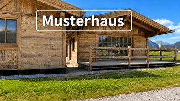 Blockhaus mit Holzfassade und kleiner Terrasse in ländlicher Umgebung unter blauem Himmel.