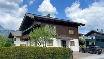 Traditionelles Einfamilienhaus mit Holzfassade und weißem Putz, umgeben von einer gepflegten Hecke.