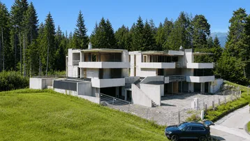 Rohbau einer modernen Wohnanlage in Betonbauweise inmitten einer grünen Berglandschaft.