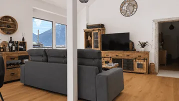 Helles Wohnzimmer mit Holzboden, gemütlichem Sofa und Bergblick durch große Fenster.