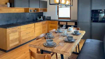 Moderne Küche mit Holzelementen, dunklen Arbeitsplatten und großem Esstisch für gemeinsame Mahlzeiten.