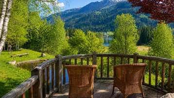 Gemütlicher Balkon mit Korbstühlen bietet einen malerischen Blick auf Berge, See und grüne Wälder.