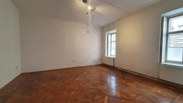 Heller Raum mit klassischem Fischgrätparkettboden und zwei hohen Fenstern, ideal für Wohnzwecke.