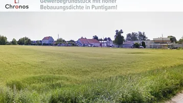 Weitläufiges Gewerbegrundstück mit grünen Feldern und vereinzelten Gebäuden im Hintergrund unter blauem Himmel.