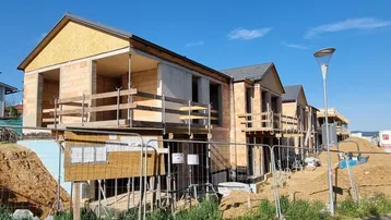 Mehrere Reihenhäuser im Rohbau auf einer Baustelle unter blauem Himmel und Sonnenschein.