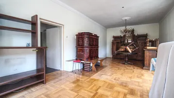 Großes Wohnzimmer mit Fischgrätparkett, Stuckdecke und einem traditionellen Kachelofen.