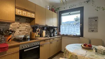 Traditionelle Einbauküche mit Essbereich, Fliesenboden und Blick auf die Berge durch das Fenster.