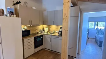 Moderne Einbauküche mit hellen Schränken, integrierten Geräten und Holzbalkendecke.