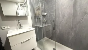 Modernes Badezimmer mit begehbarer Dusche, grauen Fliesen und weißem Waschtischunterschrank.