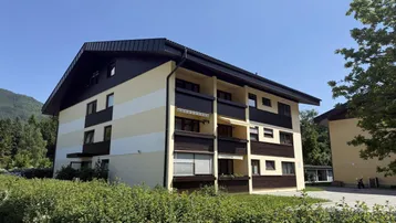 Mehrfamilienhaus mit traditioneller Architektur, Balkonen und gepflegter Außenanlage unter blauem Himmel.