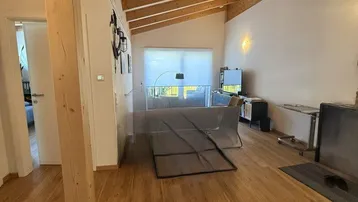 Heller Wohnbereich mit sichtbaren Holzbalken, Holzboden und einem modernen Kamin, der eine gemütliche Atmosphäre schafft.