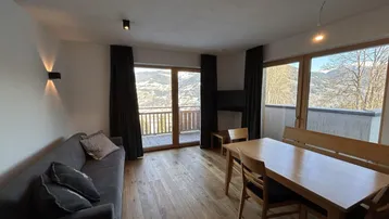 Heller Wohn- und Essbereich mit Holzboden, Zugang zum Balkon und Bergblick.