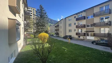 Mehrere Mehrfamilienhäuser mit Grünflächen und Bergblick unter blauem Himmel.