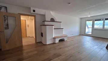 Geräumiges Wohnzimmer mit Holzboden, traditionellem Kachelofen und Zugang zum Balkon.