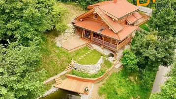 Luftaufnahme des Blockhauses mit Terrassen, Teich und umgebender Waldlandschaft.