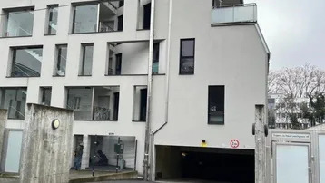 Moderne Gebäudefassade mit großen Fenstern, Balkonen und Zufahrt zur Tiefgarage.