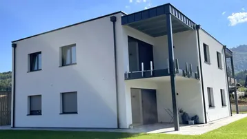 Neubau mit moderner Architektur, weißer Fassade und Balkon, umgeben von gepflegten Grünflächen.