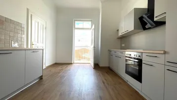 Helle Küche mit Zugang zum Balkon, ausgestattet mit modernen Geräten und Fliesenrückwand.