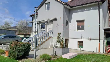 Graues Haus mit braunem Dach, Außentreppe und kleinem Gartenbereich.