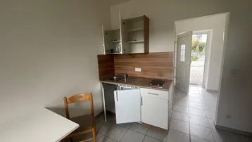 Kleine Küchenzeile mit Spüle und Kochfeld in einem hellen Raum mit Fliesenboden und Zugang nach draußen.