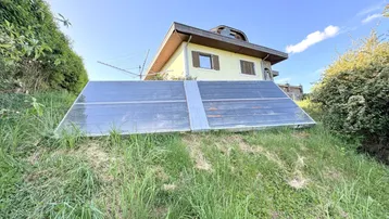 Hausansicht mit Solarpaneelen auf einem grasbewachsenen Hang im Vordergrund.