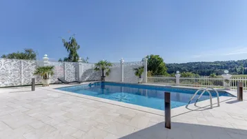 Großer Außenpool mit gefliestem Becken und umliegender Terrasse, umgeben von einer dekorativen Mauer.