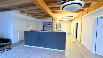 Geräumiger Empfangsbereich mit Holzbalkendecke, modernen Fliesenboden und einer dunkelblauen Theke.