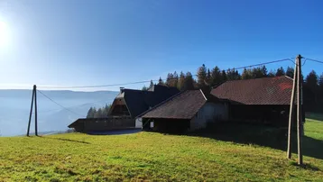 Weitläufige grüne Landschaft mit traditionellen Gebäuden und bewaldeten Hügeln unter strahlendem Himmel.