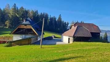 Traditionelle Gebäude in einer grünen Hügellandschaft mit Wald im Hintergrund unter blauem Himmel.