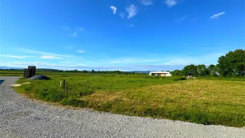 Weitläufige grüne Landschaft mit einem Haus in der Ferne unter einem klaren blauen Himmel.