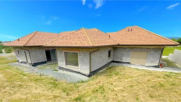 Neubau eines Einfamilienhauses mit Ziegeldach in ländlicher Umgebung unter blauem Himmel.