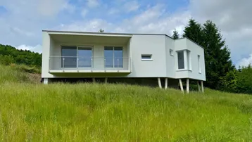 Modernes weißes Haus auf einem grünen Hügel mit Balkon und weitem Blick.