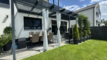 Überdachte Terrasse mit Esstisch und Stühlen, umgeben von einem gepflegten Rasenbereich.