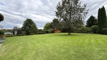 Großer, gepflegter Garten mit weitläufiger Rasenfläche, altem Baum und einem kleinen Gartenhaus.