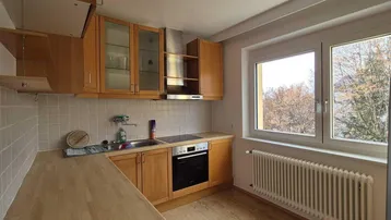 Helle Küche mit Holzschränken, Fliesenrückwand und Blick ins Grüne durch das Fenster.
