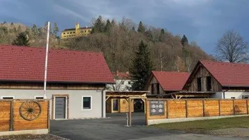 Ansicht mehrerer Häuser mit Holzzäunen und einem Hügel im Hintergrund, auf dem ein Gebäude thront.
