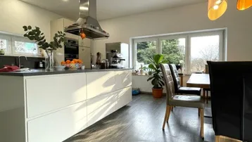 Moderne offene Küche mit Kochinsel, Essbereich und großen Fenstern mit Ausblick.