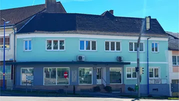 Mehrstöckiges Gebäude mit hellgrüner Fassade und Geschäften im Erdgeschoss an einer städtischen Kreuzung.