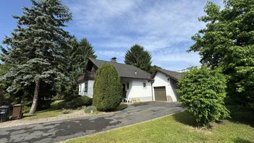 Einfamilienhaus mit Auffahrt, Garage und umgebendem Grün unter strahlend blauem Himmel.