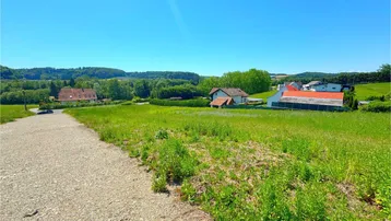 Ländliche Umgebung mit weiten Grünflächen und Häusern im Hintergrund unter blauem Himmel.