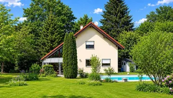 Großzügiger Gartenbereich mit Einfamilienhaus, Swimmingpool und altem Baumbestand unter blauem Himmel.