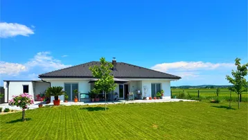 Modernes Einfamilienhaus mit großem Garten und weitem Blick ins Grüne unter blauem Himmel.