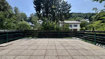 Große gepflasterte Terrasse mit Blick ins Grüne und auf umliegende Häuser.