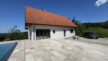 Modernes Haus mit Ziegeldach, großer gepflasterter Terrasse und einem Pool im Bau.
