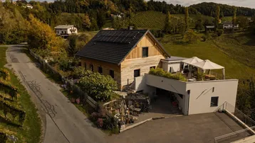 Modernes Haus mit Holzfassade, Solaranlage und großer Dachterrasse inmitten von Weinbergen.